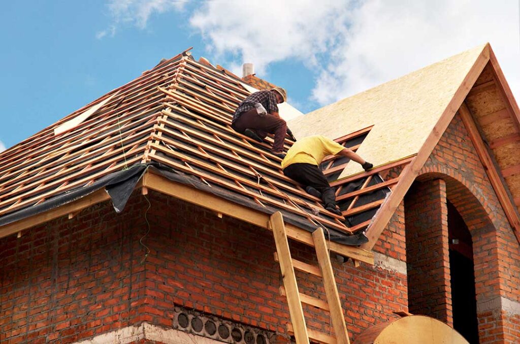 Person carefully using a secured ladder beside a dry asphalt-shingle roof with safety equipment nearby.
