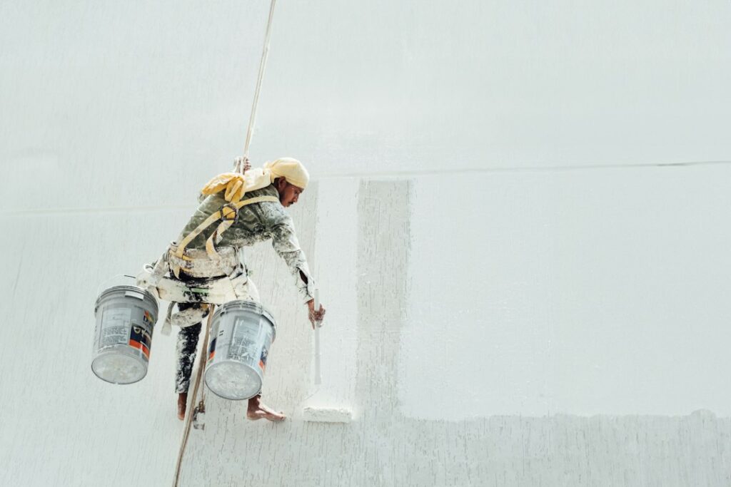A roofer applies a smooth reflective coating across a clean low-slope roof beside sealed seams and roof drains.