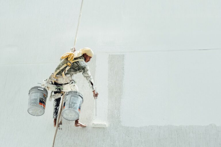A roofer applies a smooth reflective coating across a clean low-slope roof beside sealed seams and roof drains.